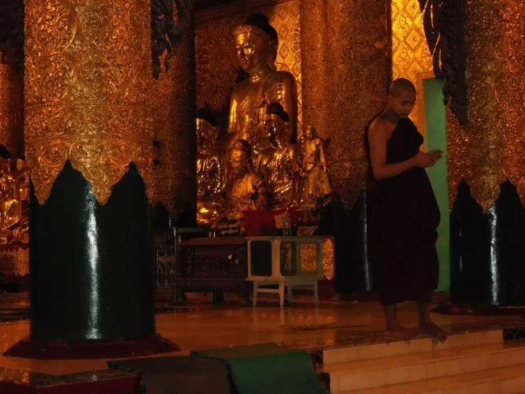 Mönch mit Smartphone vor einer Buddha-Figur bei der Shwedagon Pagode in Yangon, Myanmar/Burma