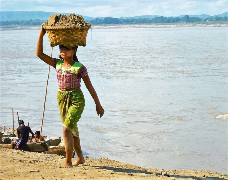 Eine Burmesin trägt einen Korb mit Sand auf dem Kopf